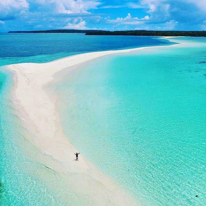 Pantai dengan pasir hitam dan air laut biru di Maluku